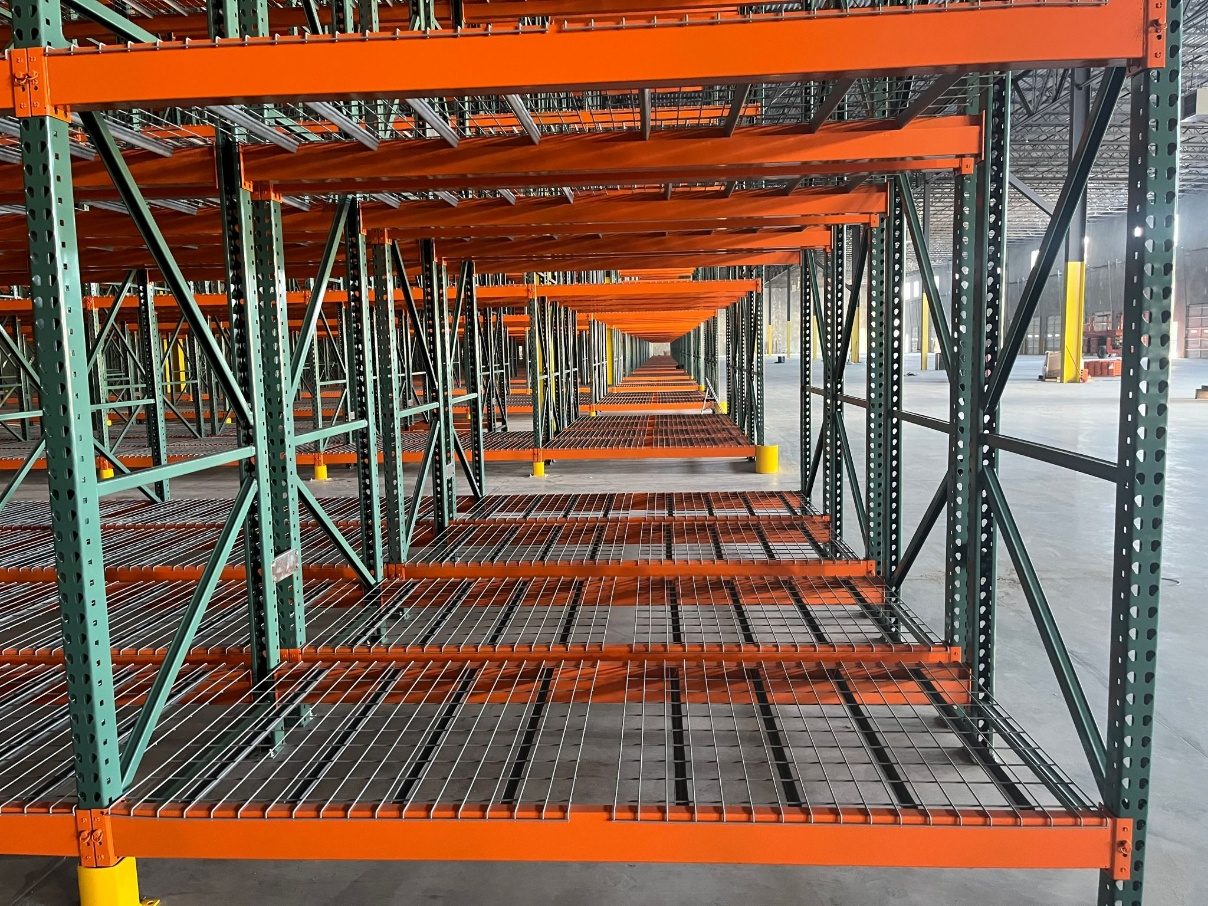 Close view through double-deep pallet rack bays showing wire decking and welded frames